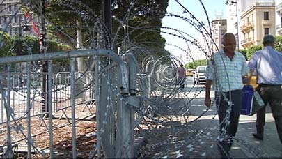 Life continues peacefully on the tree-lined boulevard, but the barbed wire remains in place.